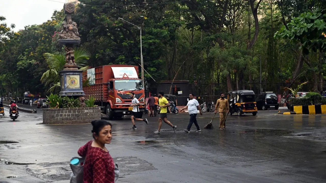 A BMC sanitation worker clears rainwater and debris from a waterlogged street after early morning showers in Kandivali East